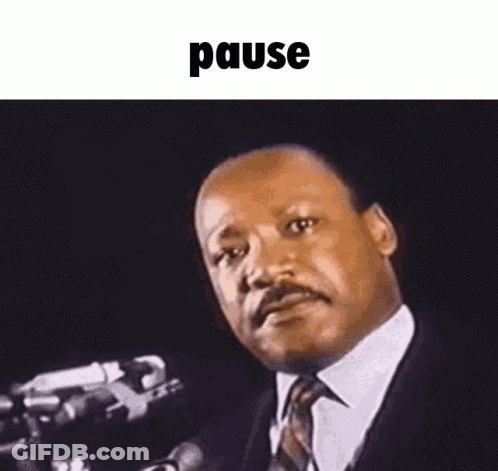 A Man In A Suit And Tie Is Standing In Front Of A Microphone And Making A Funny Face . GIF