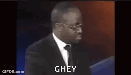 A Man In A Suit And Tie Is Standing In Front Of A Microphone And Says Ghey . GIF