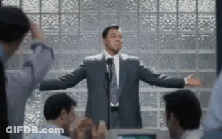 A Man In A Suit And Tie Is Standing In Front Of A Microphone Giving A Speech To A Group Of People . GIF