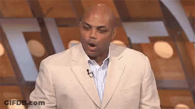 A Man In A Suit And Tie Is Standing In Front Of A Microphone With His Mouth Open . GIF