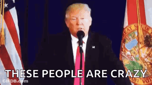 A Man In A Suit And Tie Is Standing In Front Of A Microphone With The Words `` These People Are Crazy '' . GIF