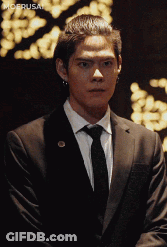 A Man In A Suit And Tie Is Standing In Front Of A Moerusai Logo GIF