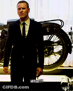 A Man In A Suit And Tie Is Standing In Front Of A Motorcycle And Says What GIF