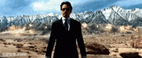 A Man In A Suit And Tie Is Standing In Front Of A Mountain Range GIF