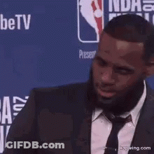 A Man In A Suit And Tie Is Standing In Front Of A Nba Finals Sign GIF