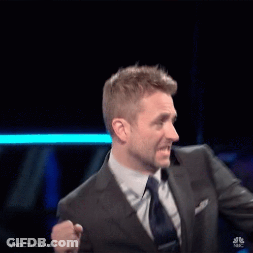 A Man In A Suit And Tie Is Standing In Front Of A Nbc Sign GIF