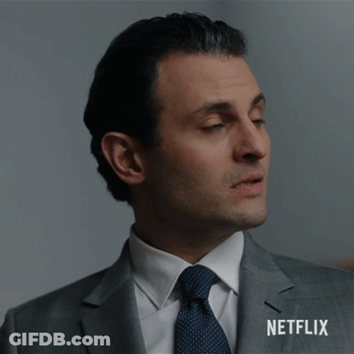 A Man In A Suit And Tie Is Standing In Front Of A Netflix Sign GIF