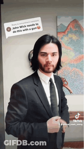 A Man In A Suit And Tie Is Standing In Front Of A Painting That Says John Wick GIF