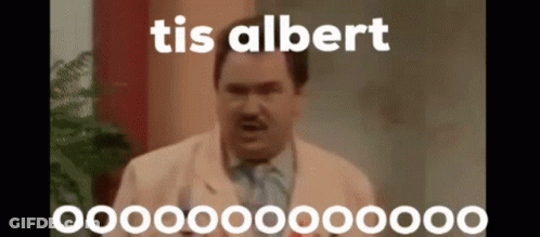 A Man In A Suit And Tie Is Standing In Front Of A Plant And Talking . GIF