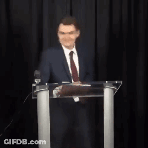 A Man In A Suit And Tie Is Standing In Front Of A Podium With His Arms Outstretched . GIF