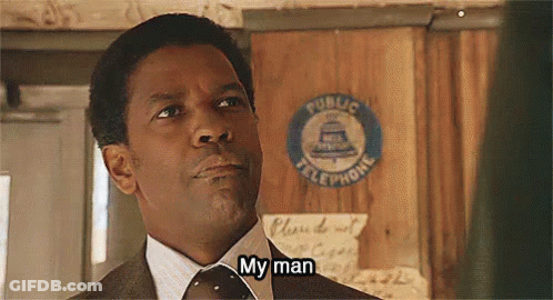 A Man In A Suit And Tie Is Standing In Front Of A Public Telephone Sign And Saying `` My Man '' . GIF
