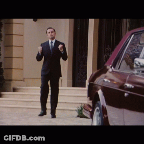 A Man In A Suit And Tie Is Standing In Front Of A Red Car GIF