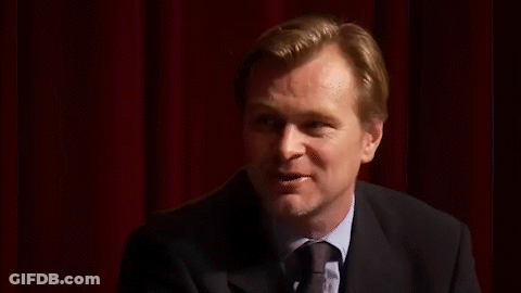 A Man In A Suit And Tie Is Standing In Front Of A Red Curtain And Smiling . GIF