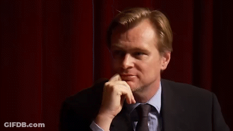A Man In A Suit And Tie Is Standing In Front Of A Red Curtain . GIF