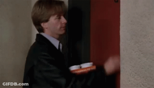 A Man In A Suit And Tie Is Standing In Front Of A Red Door Holding A Tray Of Pills . GIF