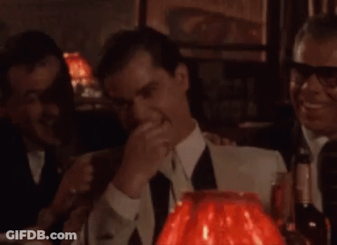 A Man In A Suit And Tie Is Standing In Front Of A Red Lamp In A Bar . GIF