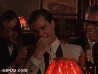 A Man In A Suit And Tie Is Standing In Front Of A Red Lamp . GIF
