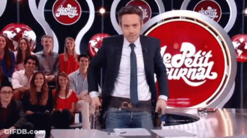 A Man In A Suit And Tie Is Standing In Front Of A Red Sign That Says Le Petit Journal GIF