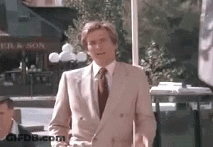 A Man In A Suit And Tie Is Standing In Front Of A Restaurant . GIF