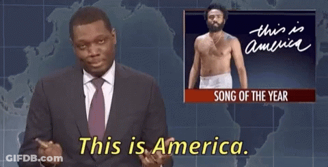 A Man In A Suit And Tie Is Standing In Front Of A Screen That Says This Is America GIF