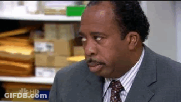 A Man In A Suit And Tie Is Standing In Front Of A Shelf . GIF