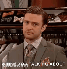 A Man In A Suit And Tie Is Standing In Front Of A Shelf Of Ties . GIF