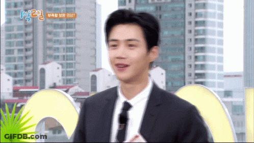 A Man In A Suit And Tie Is Standing In Front Of A Sign That Says 1 2 GIF