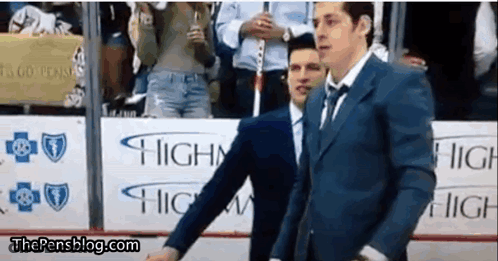 A Man In A Suit And Tie Is Standing In Front Of A Sign That Says Highway . GIF