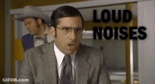 A Man In A Suit And Tie Is Standing In Front Of A Sign That Says Loud Noises GIF
