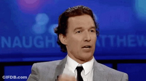 A Man In A Suit And Tie Is Standing In Front Of A Sign That Says Naughey Matthew GIF