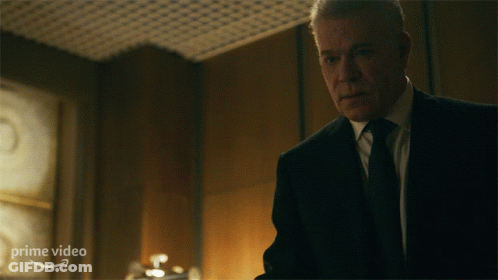 A Man In A Suit And Tie Is Standing In Front Of A Sign That Says Prime Video On It GIF