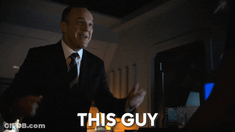 A Man In A Suit And Tie Is Standing In Front Of A Sign That Says This Guy GIF