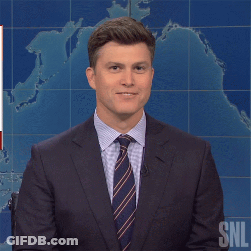 A Man In A Suit And Tie Is Standing In Front Of A Snl Sign GIF