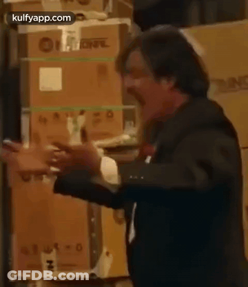 A Man In A Suit And Tie Is Standing In Front Of A Stack Of Boxes . GIF