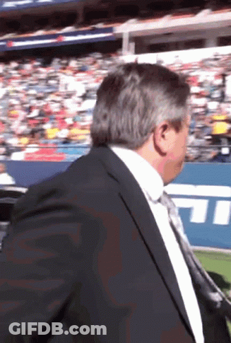 A Man In A Suit And Tie Is Standing In Front Of A Stadium With The Letters Tnt On It GIF