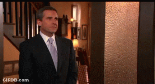 A Man In A Suit And Tie Is Standing In Front Of A Staircase GIF
