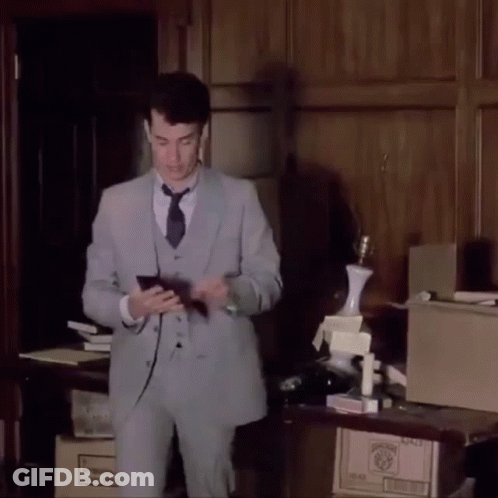 A Man In A Suit And Tie Is Standing In Front Of A Table With Boxes On It And A Lamp On Top GIF