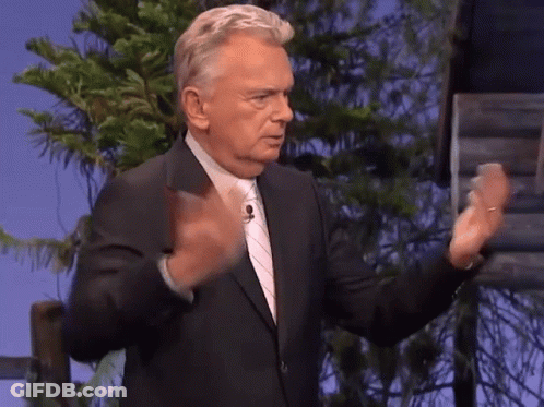 A Man In A Suit And Tie Is Standing In Front Of A Tree GIF