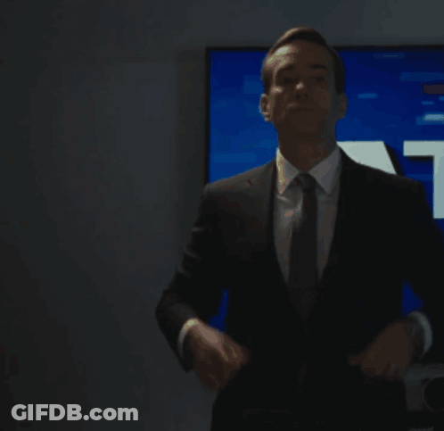 A Man In A Suit And Tie Is Standing In Front Of A Tv Screen With The Letter A In White GIF