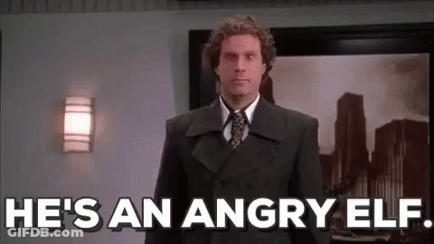A Man In A Suit And Tie Is Standing In Front Of A Wall And Says `` He 'S An Angry Elf '' . GIF