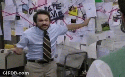 A Man In A Suit And Tie Is Standing In Front Of A Wall Covered In Posters . GIF
