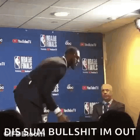 A Man In A Suit And Tie Is Standing In Front Of A Wall That Says Nba Finals GIF