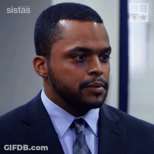 A Man In A Suit And Tie Is Standing In Front Of A Wall That Says Sistas GIF