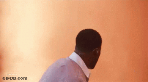 A Man In A Suit And Tie Is Standing In Front Of A Wall With A Blurred Background . GIF