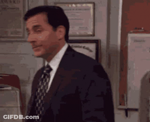 A Man In A Suit And Tie Is Standing In Front Of A Wall With Awards On It . GIF
