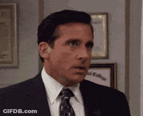 A Man In A Suit And Tie Is Standing In Front Of A Wall With Framed Pictures On It . GIF