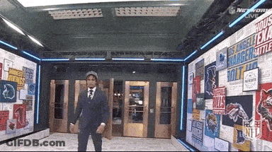 A Man In A Suit And Tie Is Standing In Front Of A Wall With Nfl Logos GIF