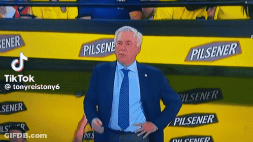 A Man In A Suit And Tie Is Standing In Front Of A Wall With Pilsener Advertisements GIF