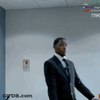 A Man In A Suit And Tie Is Standing In Front Of A Wall With The Words Fired On It GIF