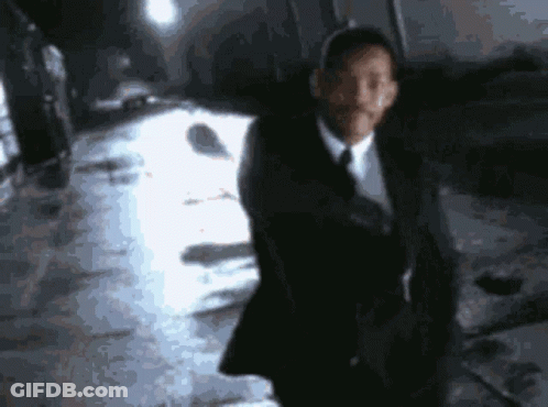 A Man In A Suit And Tie Is Standing In Front Of A White Car GIF